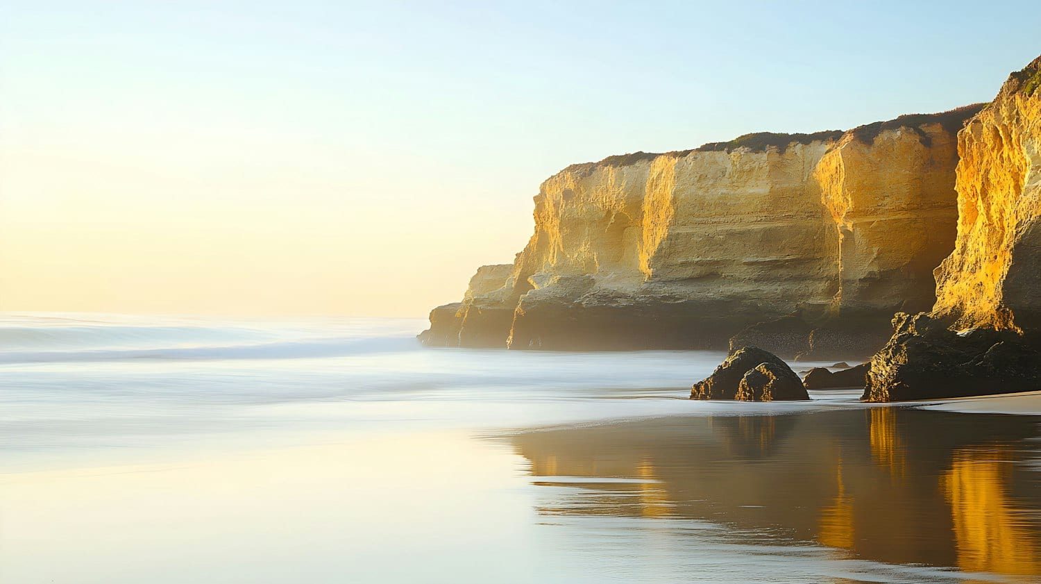 Golden limestone cliffs above a calm beach in early morning light